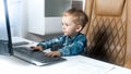 Little smart toddler boy sitting in office and working on computer