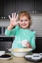 Little smilig girl having fun cooking in kitchen. Small child mixing dough, showing hand with flour.