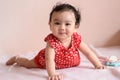 Little smiling Asian baby, a cute toddler dressed in red practicing crawling on the bed and looking at the camera