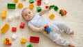 Little smiling baby boy on carpet in playroom covered with colroful toys, bricks and blocks. Concept of children Royalty Free Stock Photo