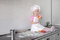 Little smiling baby girl baker in white cook hat and apron kneads a dough on tle kitchen Royalty Free Stock Photo