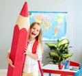 Little smiling blond girl holding huge red pencil in the school classroom Royalty Free Stock Photo