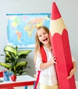 Little smiling blond girl holding huge red pencil in the school classroom Royalty Free Stock Photo