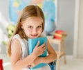 Little smiling blond girl holding blue book in the school class