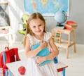 Little smiling blond girl holding blue book in the school class