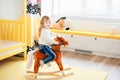 Little smiling blonde 3 years old girl sitting on rocking horse in yellow bedroom at home in day time. Time to play during self