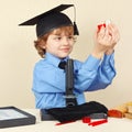 Little smiling boy in academic hat conducts scientific research with microscope Royalty Free Stock Photo