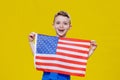 Little smiling boy holding an American flag on a yellow background. Patriotism, independence day, flag day concept Royalty Free Stock Photo