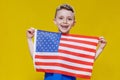 Little smiling boy holding an American flag on a yellow background. Patriotism, independence day, flag day concept Royalty Free Stock Photo