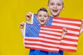 Little smiling boy holding an American flag on a yellow background. Patriotism, independence day, flag day concept Royalty Free Stock Photo