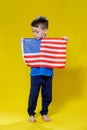 Little smiling boy holding an American flag on a yellow background. Patriotism, independence day, flag day concept Royalty Free Stock Photo