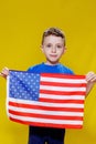 Little smiling boy holding an American flag on a yellow background. Patriotism, independence day, flag day concept Royalty Free Stock Photo