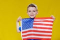 Little smiling boy holding an American flag on a yellow background. Patriotism, independence day, flag day concept Royalty Free Stock Photo