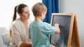 Little smiling boy learning ABC with young mother at home. Teacher writing alphabet on blackboard with chalk. Home Royalty Free Stock Photo