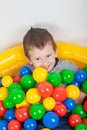 Little smiling boy playing lying in colorful balls playground