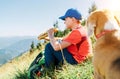 Little smiling boy weared baseball cap enjoying a huge baguette sandwich and his beagle dog friend watching it during a mountain