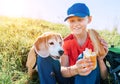 Little smiling boy weared baseball cap sharing a huge baguette sandwich with his beagle dog friend during a mountain hiking Royalty Free Stock Photo