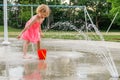 Little smiling child playing at water splash pad fountain in the park playground during hot summer day Royalty Free Stock Photo