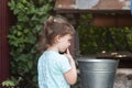 Little smiling country girl looks thoughtfully at the metal bucket on the well