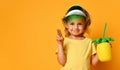 Little smiling cute blond girl in yellow t-shirt and hat holding fresh healthy fruit juice in pineapple shaped bottle with straw Royalty Free Stock Photo