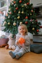 Little smiling girl with a ball in her hands sits on the floor near the Christmas tree Royalty Free Stock Photo