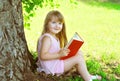 Little smiling girl child reading a book on the grass near tree