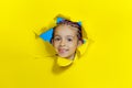 Little smiling girl looking out of a hole in a yellow paper. Horizontal view. Copy space. Royalty Free Stock Photo