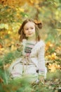 Little smiling girl sitting on a plaid in an autumn park. Cute Caucasian girl in autumn park holding yellow maple leaf in hand