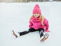 Little smiling girl skate and fell on ice in pink wear. Outdoor.