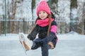 Little smiling girl skating on ice in pink wear. winter