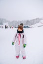 Little smiling girl stands on a snowy ski slope against the backdrop of skiers
