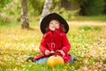 Little girl wearing Halloween witch hat and warm red coat, having fun in the park, autumn day. Royalty Free Stock Photo