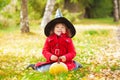 Little girl wearing Halloween witch hat and warm red coat, having fun in the park, autumn day. Royalty Free Stock Photo