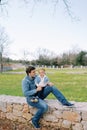 Little smiling girl in a wreath sits on her dad knees on a stone fence in a clearing Royalty Free Stock Photo