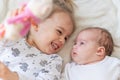 Little smiling kids playing together sitting on the bed. Brother and sister show a newborn a toy. Toddler kids meeting Royalty Free Stock Photo