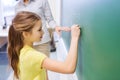 Little smiling schoolgirl writing on chalk board