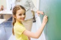 Little smiling schoolgirl writing on chalk board