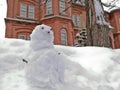 Little snow man doll with curious face and red brick vintage building