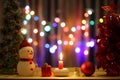 Little snow man with lit red candle light Christmas scenic on wooden table and colorful bokeh background Royalty Free Stock Photo