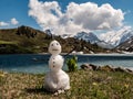 Little snowman melting during spring with mountain scenery behind