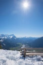 Little snowman sitting on a wooden bench, looking intothe landscape of bavarian alps. bright sunshine