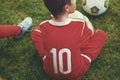 Little soccer forward player boy sitting on grass
