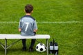Little soccer player sitting on a wooden bench and watching soccer game Royalty Free Stock Photo