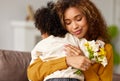 Young mixed race woman mother with flower bouquet embracing son while getting congratulations on Mother`s day Royalty Free Stock Photo