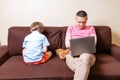 Little Son Offended To His Father Busy With Laptop. Man and kid boy sitting on couch. Cute child sitting back and angry