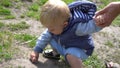 Little son tryng to touch an ant on ground in park at sunny day with a little help from his father