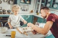 Little son using baking tins while forming cookies with father