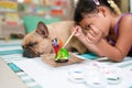 Little Southeast Asian girl painting a dog figurine next to sleeping a French bulldog indoors