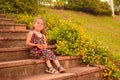 Little Spanish kid with a cute face posing for a picture in a park while sitting on the stairs