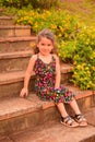 Little Spanish kid with a cute face posing for a picture in a park while sitting on the stairs